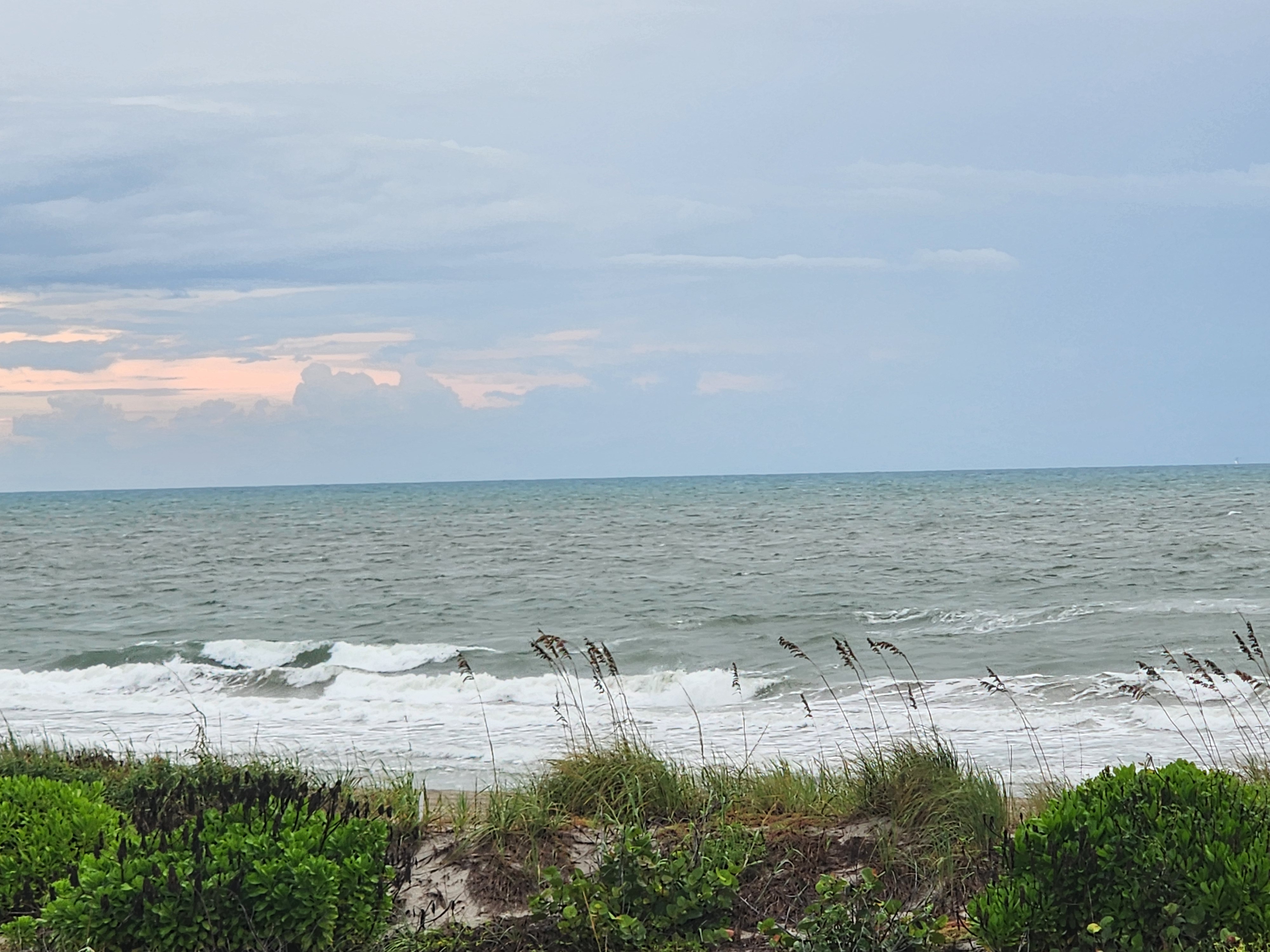 Messy shorebreak and whitecaps offshore under layered storm clouds