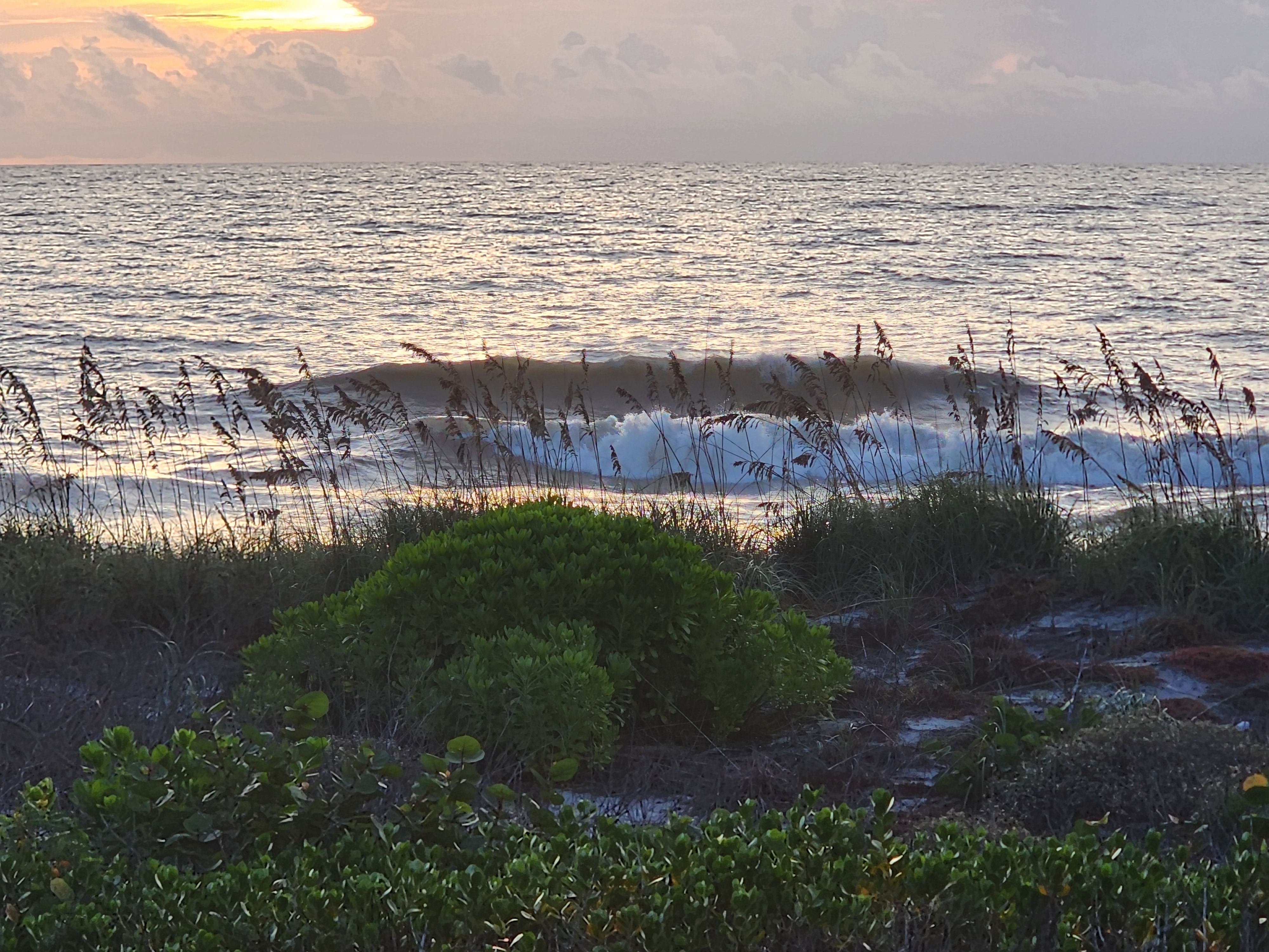 A shoulder-high set wave feathering and breaking with a bright sunrise glow breaking through the clouds