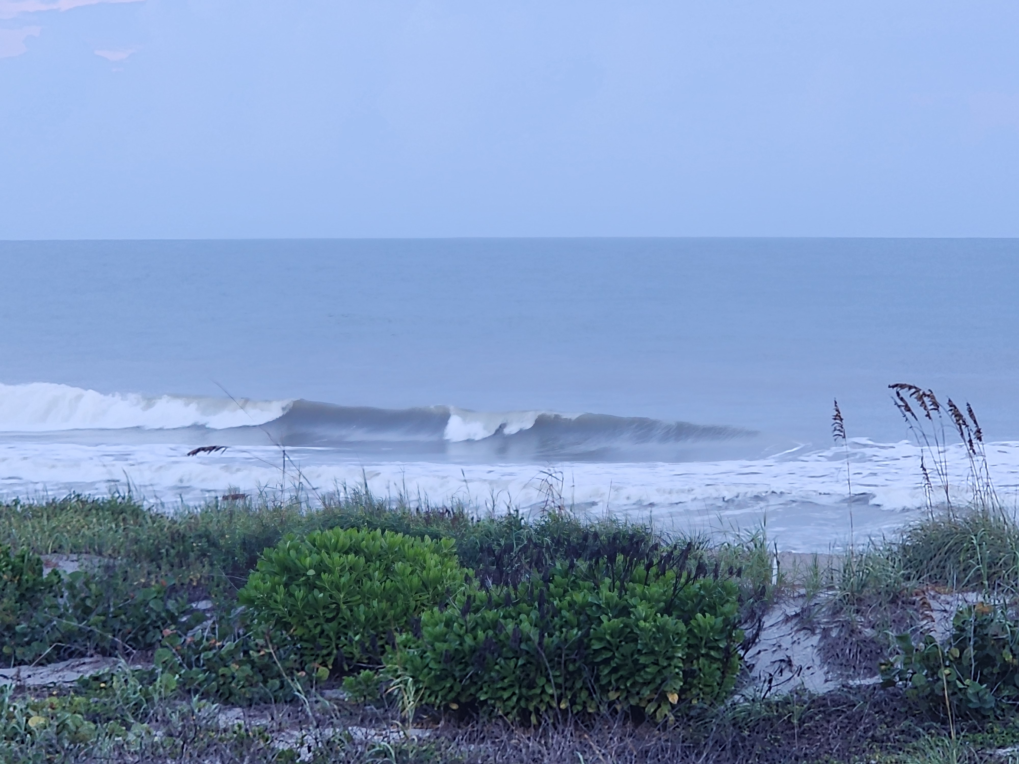 A glassy set wave peeling along the sandbar with whitewater rolling in on the high tide