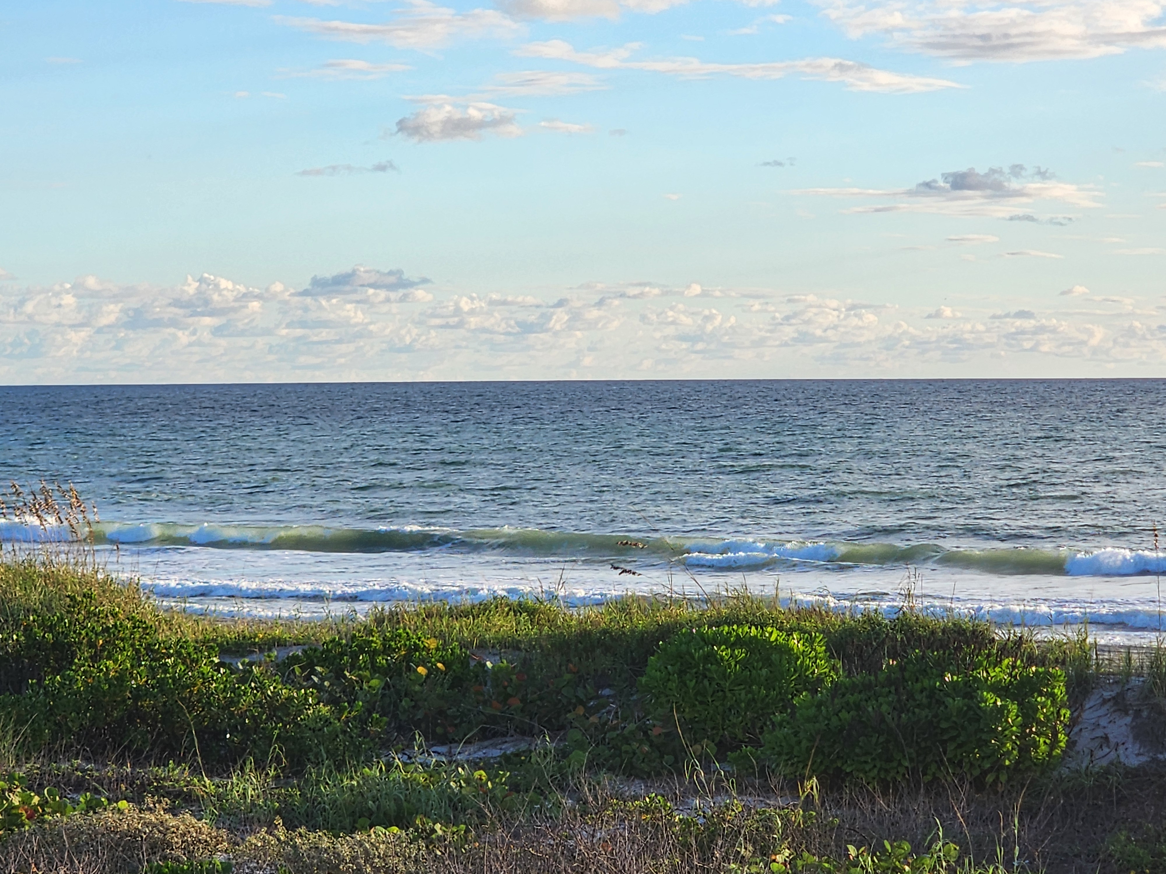 Green-tinged waves breaking in a long line across the inside, blue sky with scattered clouds