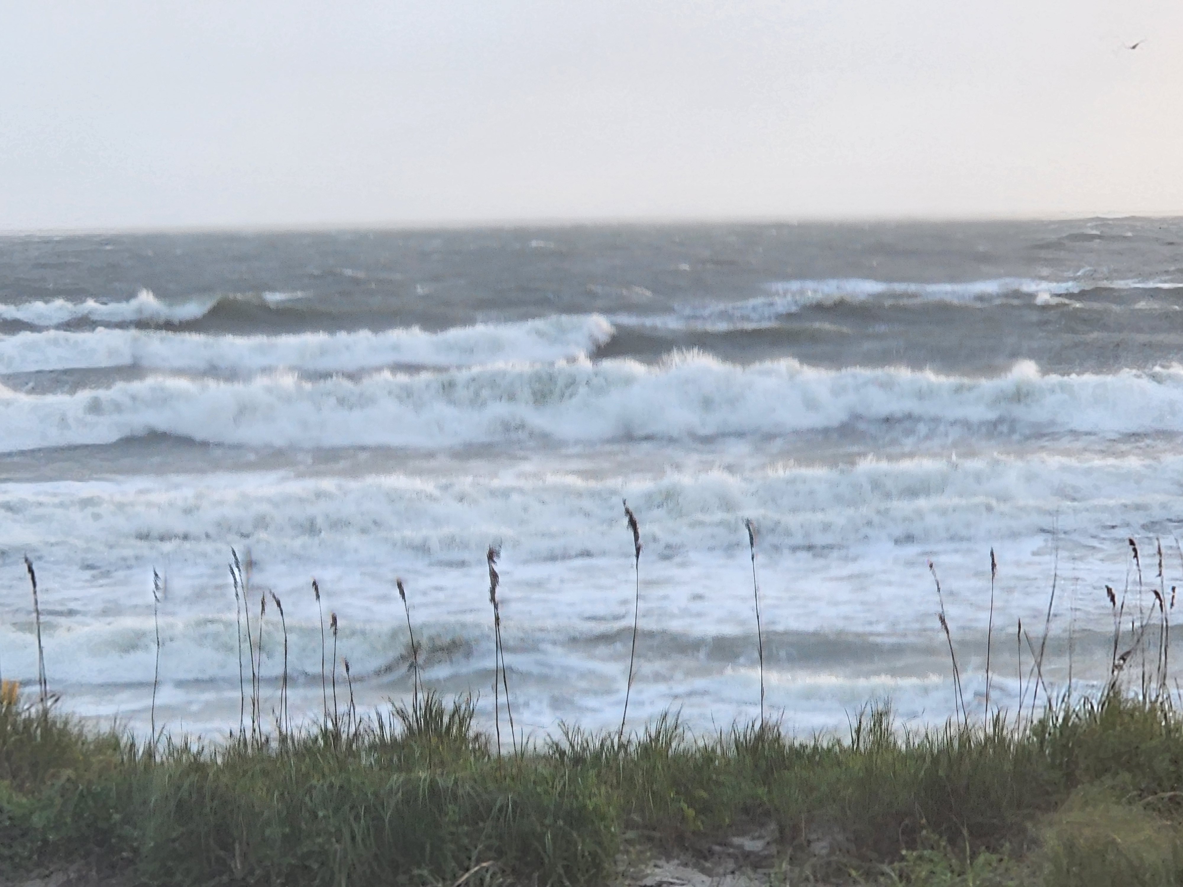 Wall-to-wall whitewater with stacked, wind-torn breakers rolling toward shore beneath a pale gray sky