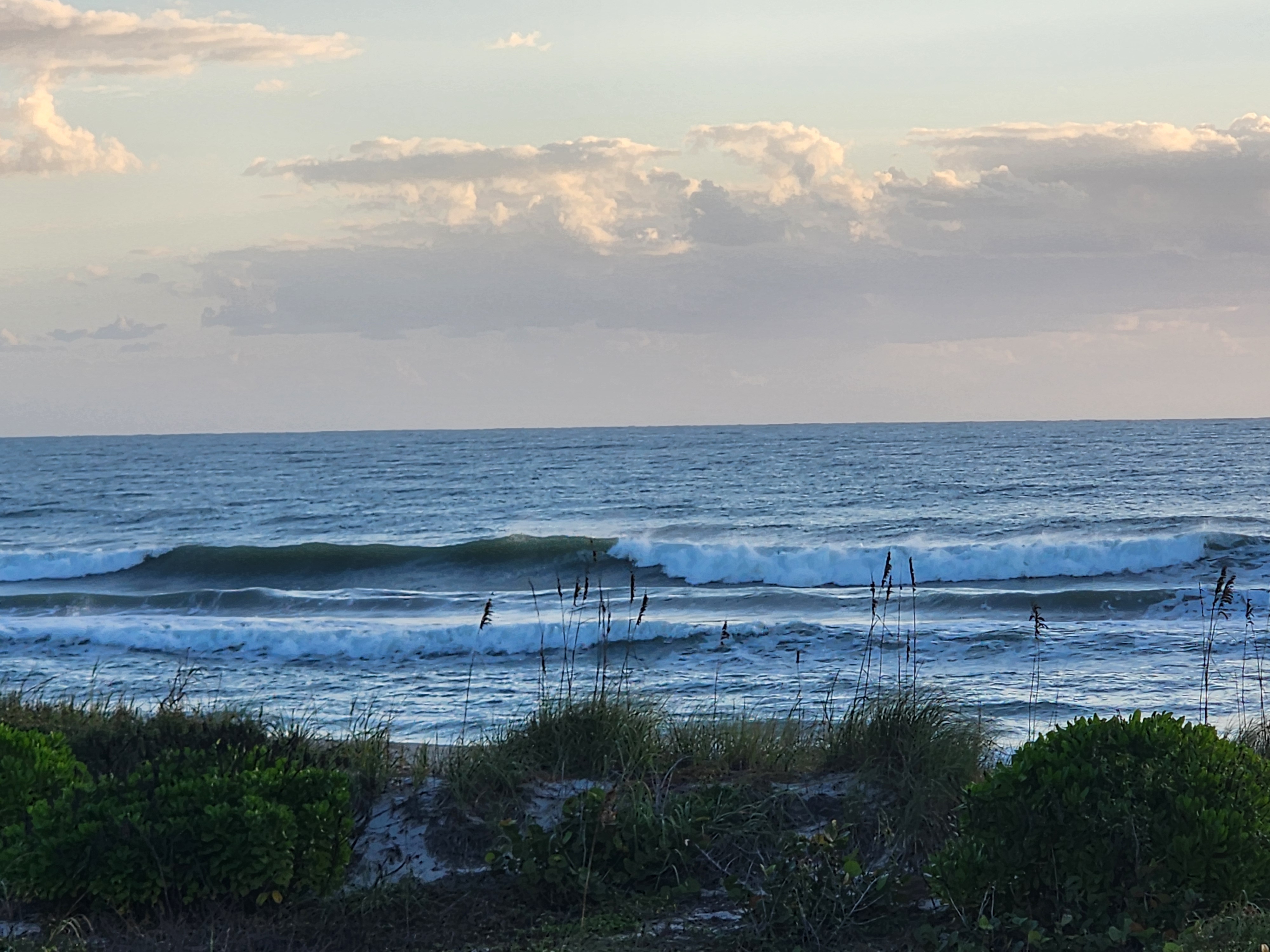 A smooth dark-green left peeling long down the line with whitewater on the inside and puffy clouds overhead