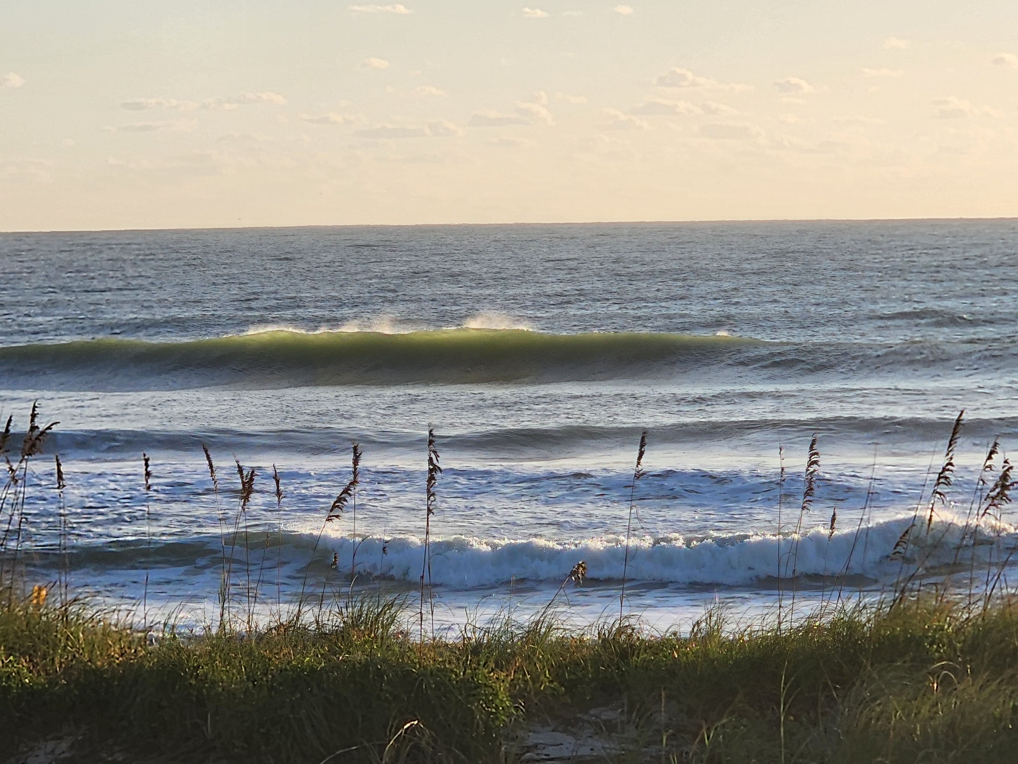 Glassy green wall of a set wave feathering with offshore spray beyond the inside whitewater