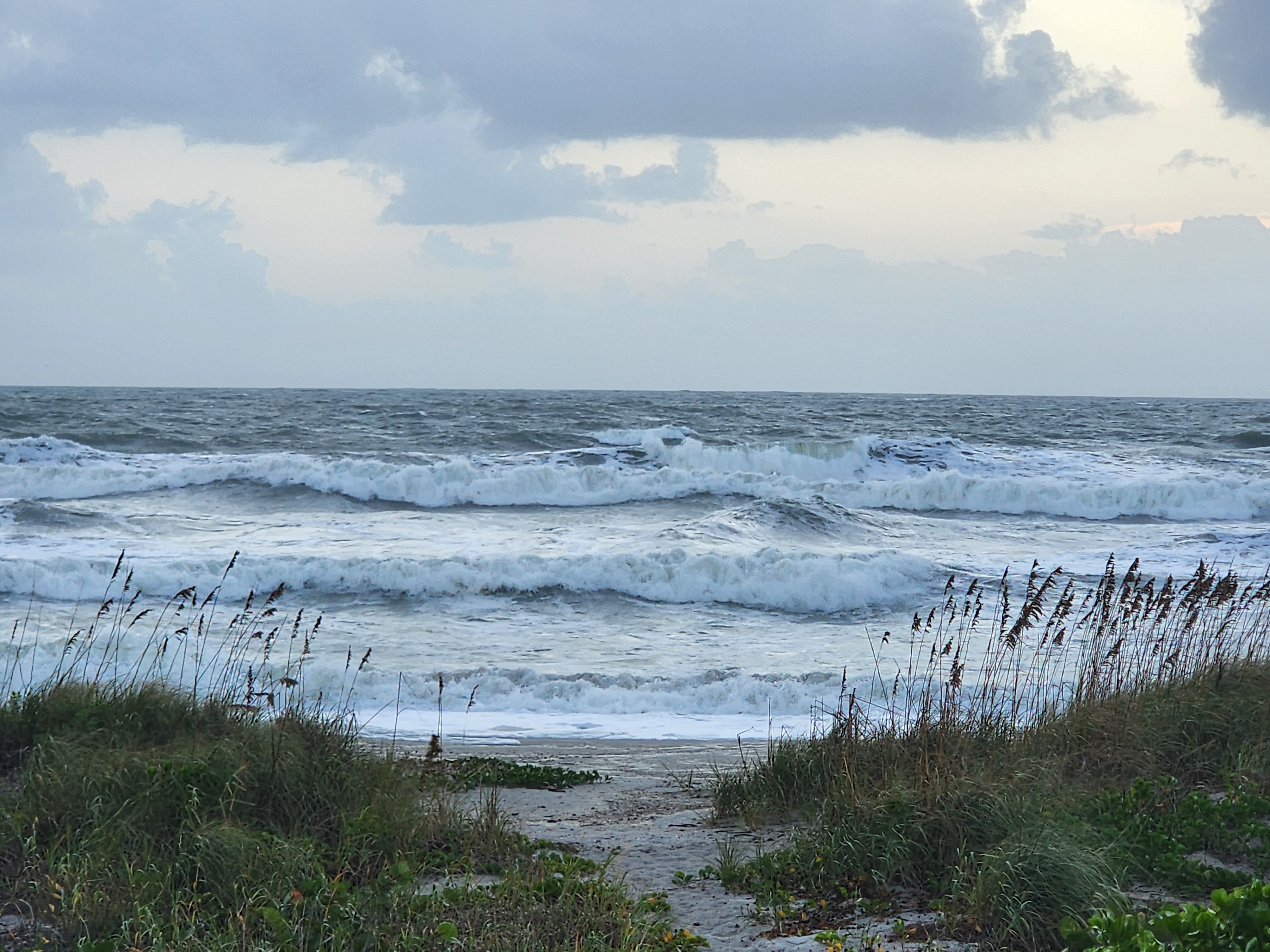 Multiple lines of breaking waves and foam filling the water right up to the end of the dune path